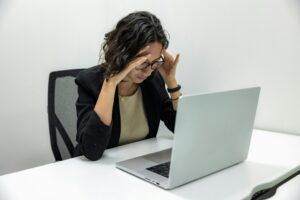 A young woman experiencing stress and fatigue while working on her laptop in an office setting.