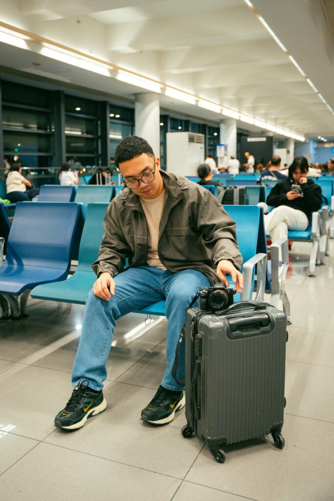 Young traveler sitting in airport terminal with luggage and camera, awaiting departure.
