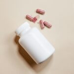 Close-up shot of a white pill bottle and red capsules on a beige background, ideal for healthcare themes.
