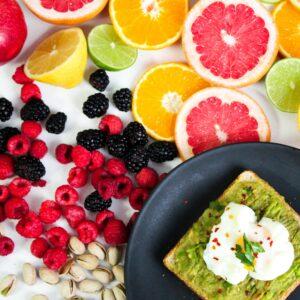 Colorful avocado toast with assorted fresh fruits including citrus, berries, and pistachios.
